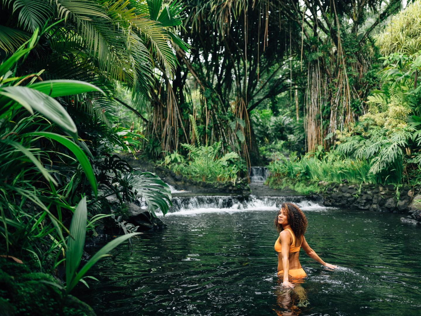 woman in waterfall pool in forest